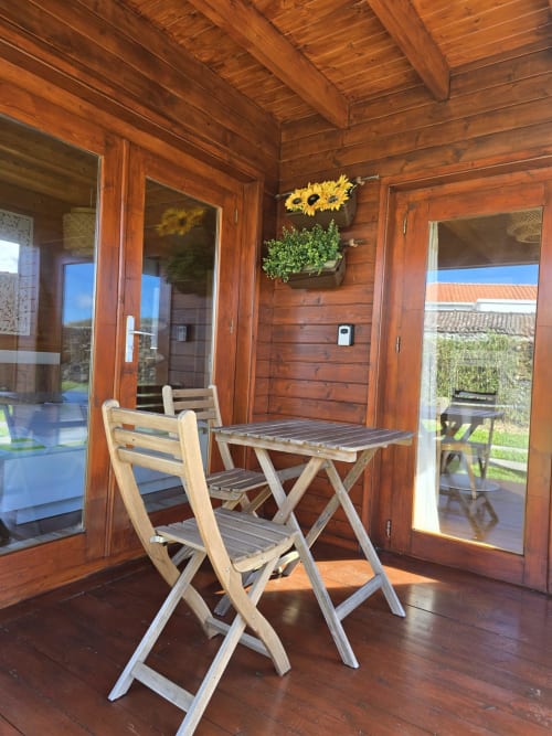 Wooden cabin interior with folding chairs and table at Mountain Wood Village apartment in Madalena, featuring sunlit windows