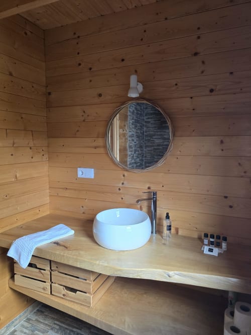 Rustic wooden bathroom in Mountain Wood Village apartment with round white sink, circular mirror, and natural wood vanity