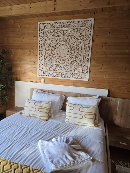 Cozy bedroom at Mountain Wood Village with carved wooden wall panel, white bed, gold-patterned pillows, and pine wood walls.