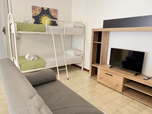 Soggiorno moderno con letti a castello, divano grigio, TV e arredi in legno presso Poseidon Bay Residence, Milazzo