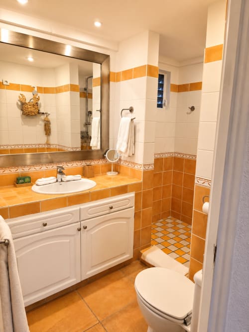 Salle de bain moderne avec carrelage orange et blanc, vasque blanche, toilettes et douche aux Balcons d'Oyster Pond, Saint-Martin