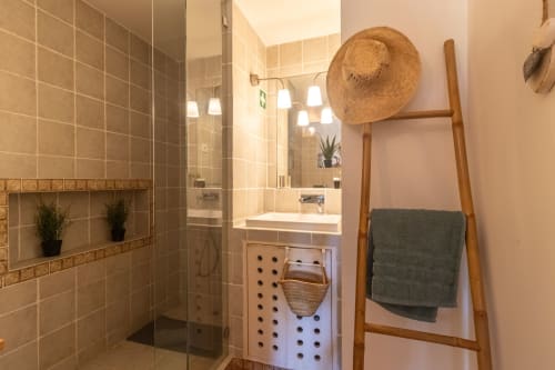 Baño moderno con ducha de azulejos, lavamanos blanco, toallero de escalera de madera y plantas en macetas en Urban Beach Rentals