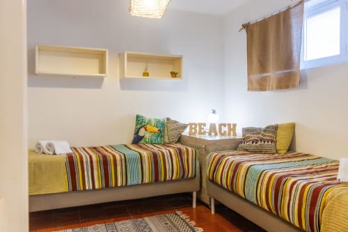 Habitación luminosa con camas gemelas, ropa de cama a rayas coloridas, decoración de playa y estantes de madera en Urban Beach Rentals