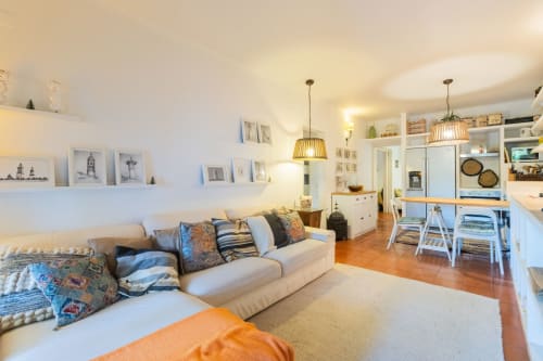 Luminoso salón con sofá beige, pisos de madera, lámparas colgantes y almacenamiento blanco en Urban Beach