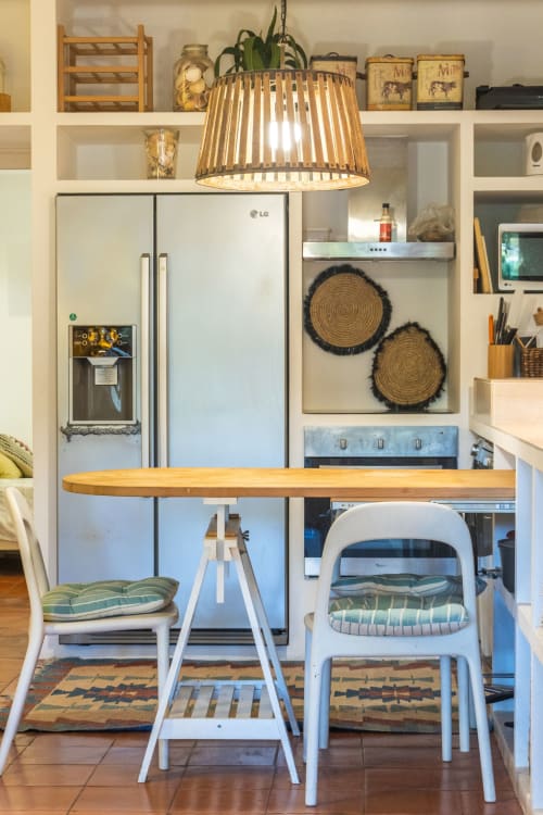 Moderna cocina con encimera de madera, sillas blancas, lámpara de tejido trenzado y electrodomésticos de acero inoxidable en apartamento de Albufeira.