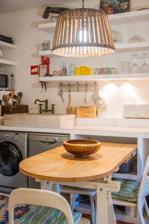 Cocina moderna con lámpara colgante de madera, estanterías blancas, mesa de comedor de madera con cuenco, lavadora y estufa