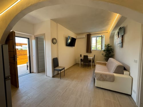 Camera Elisabetta al Queen Hotel Campofilone: ampio monolocale con pareti beige, divano crema, tavolo da pranzo, TV, illuminazione moderna,