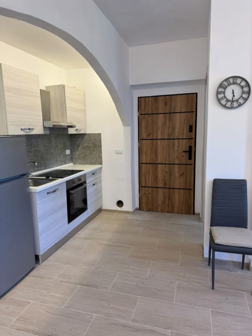Cucina moderna nella camera Elisabetta dell'Hotel Queen a Campofilone, con mobili bianchi, rivestimento grigio, porta in legno e