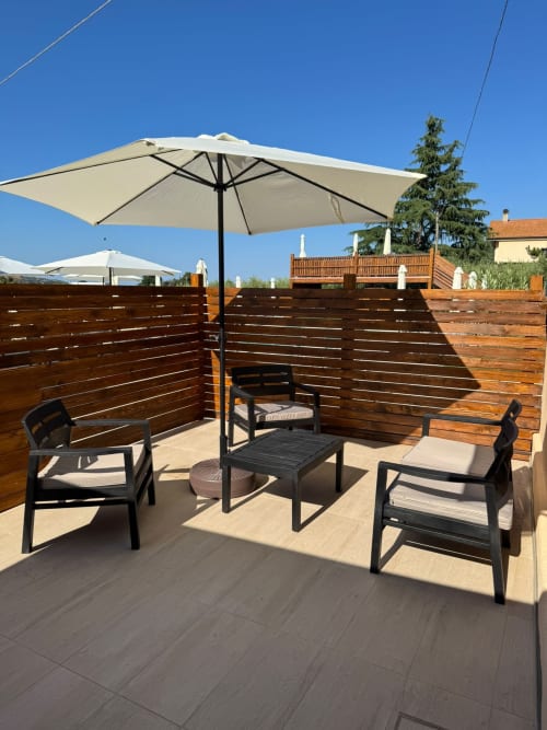 Terrazza esterna del Queen Hotel a Campofilone con ombrellone, sedie nere e schermi in legno sotto cielo azzurro