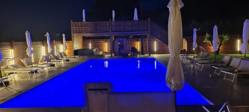 Piscina illuminata di blu la notte con lettini, ombrelloni e edificio in legno della Queen Hotel a Campofilone