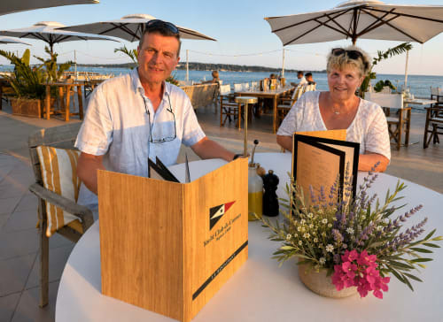 Deux hôtesses dans un restaurant en bord de mer à Cannes tenant des menus avec vue sur la Méditerranée et parasols