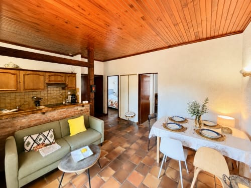 Cuisine ouverte et salle à manger avec plafond bois, canapé vert et table dressée à Mimizan Plage