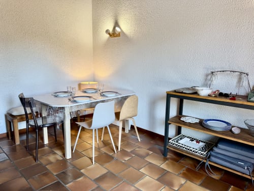 Salle à manger lumineuse dans l'appartement de Mimizan Plage avec table blanche, chaises modernes, étagères en bois et carrelage en terre cuite.