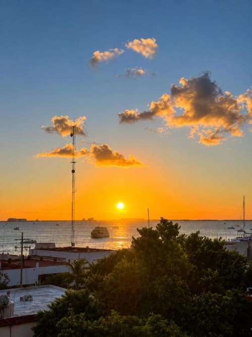 Atardecer en la bahía de Isla Mujeres con embarcaciones, palmeras y torre de antena del Hotel Isla Mujeres Centro