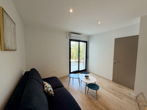 Suite moderne avec canapé noir, parquet, portes donnant sur le jardin et mobilier contemporain à CARPE DIEM Résidence