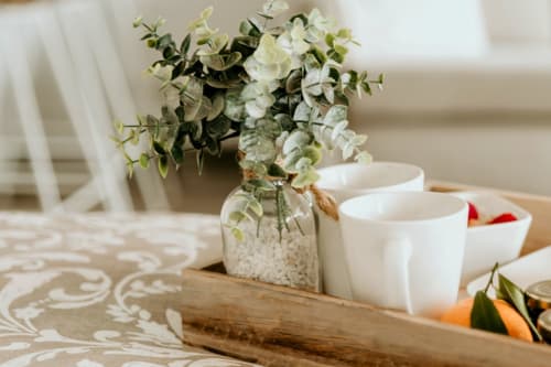 Elegant table setting at Sable & Pampas with white cups, eucalyptus flowers in glass vase, and wooden tray at Carnon-Plage