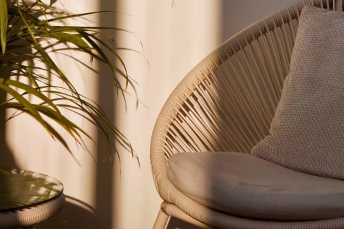 Woven chair with linen cushion beside potted plant at Sable & Pampas, Carnon-Plage