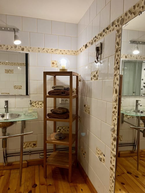 Salle de bains moderne avec carreaux blancs métro, accents de galets, étagère en bois, vasques doubles et porte-serviettes chauffants