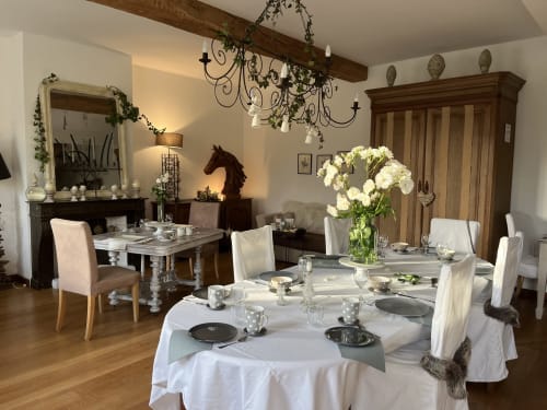 Salle à manger élégante du Domaine De La Ferme avec table ronde, linge blanc, cheminée et vue sur le jardin