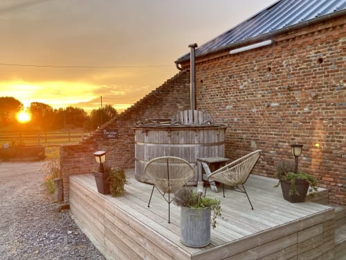 Vue au coucher de soleil de la terrasse en bois avec chaises, bain à remous et maison de ferme en brique au Domaine De La Ferme De Ribeaufontaine, Dorengt