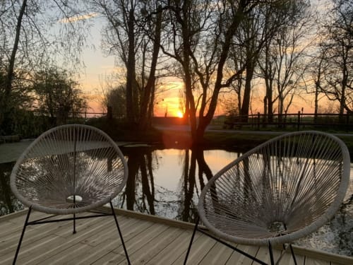Vue du coucher de soleil depuis la terrasse en bois avec chaises tissées surplombant l'étang au Domaine De La Ferme De Ribeaufontaine