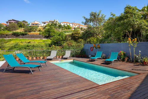 Espreguiçadeiras turquesas e piscina retangular no deck de madeira da villa Paradise House Calheta com vista para a aldeia na encosta