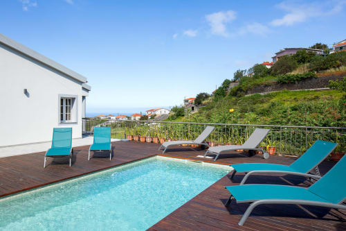Espreguiçadeiras turquesas à beira da piscina com vista para a costa de Calheta na Villa Paradise House
