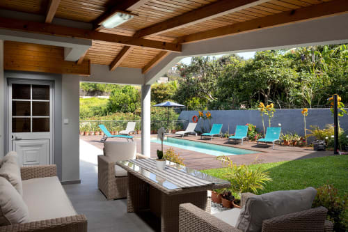 Pátio da Villa Paradise House Calheta com espreguiçadeiras turquesas, piscina, pérgula de madeira e vista para jardim luxuriante