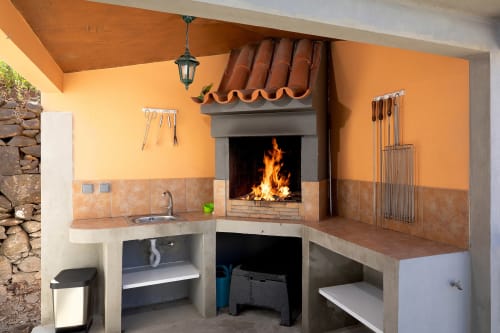 Pavilhão de cozinha ao ar livre com lareira, pia e área de refeições na villa Paradise House Calheta, Portugal