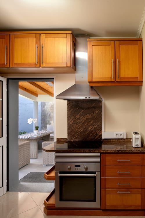 Cozinha moderna com armários de madeira, eletrodomésticos em aço inoxidável e bancada em granito na villa Paradise House Calheta