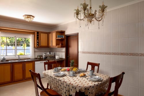 Sala de jantar elegante com mesa e cadeiras em madeira, lustre, cozinha moderna e vistas para o oceano na villa Paradise House Calheta