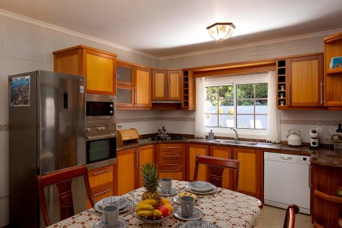 Cozinha moderna com armários em madeira, eletrodomésticos em aço inoxidável e mesa de jantar na villa Paradise House em Calheta, Portugal