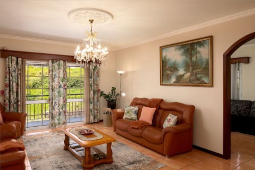 Elegante sala de estar da villa Paradise House Calheta com sofá de couro, lustre e vista para o terraço