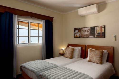 Duas camas de solteiro com cabeceiras em madeira no quarto da villa Paradise House Calheta, com unidade de ar condicionado e arte de Buda