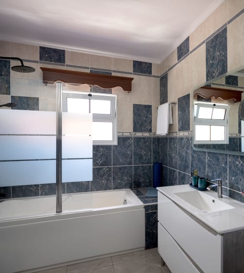 Banheiro moderno da vila Paradise House Calheta com azulejos de mármore escuro, duas pias, banheira e chuveiro com box em vidro