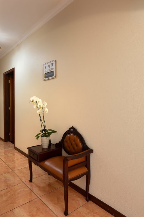 Elegante corredor da villa Paradise House Calheta com orquídea branca, poltrona de couro e placa com senha WiFi