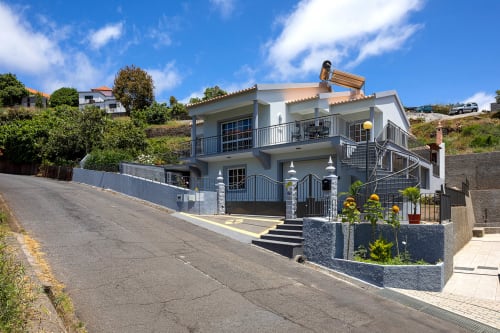 Villa Paradise House Calheta com arquitetura moderna, fachada branca, guarda-corpos azuis e detalhes em pedra na encosta
