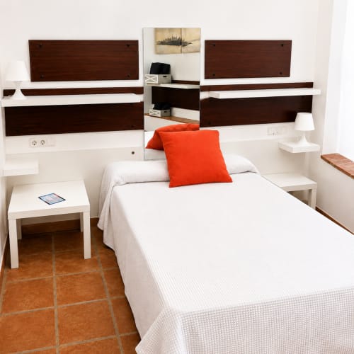 Modern bedroom with white and dark wood furniture, red pillow, terracotta floor at Apartamentos Turísticos Axarent, Málaga