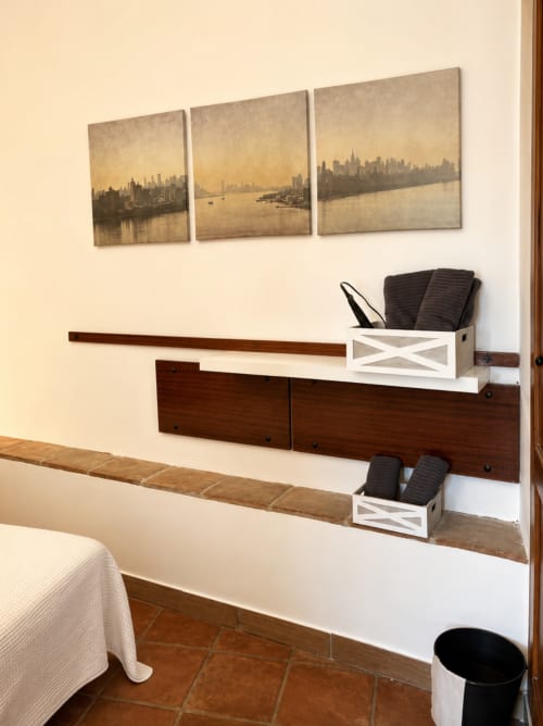Modern bedroom in Málaga apartment with wall-mounted shelving, dark wood headboard, white storage boxes, and three framed
