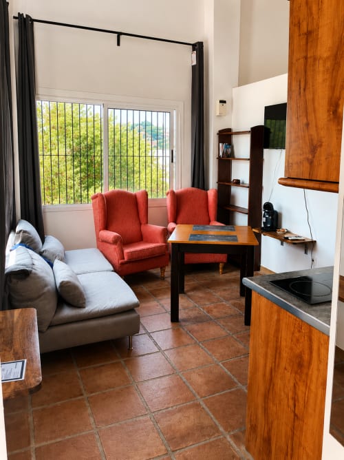 Modern Málaga apartment living room with red armchairs, gray sofa, terracotta tile floor, and sea views through large windows