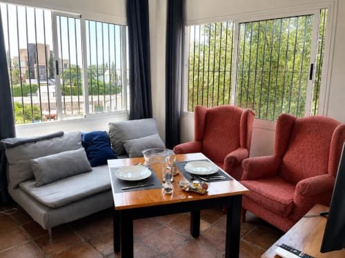 Modern living room in Málaga apartment with gray sofa, red armchairs, wooden table, and sea views through floor-to-ceiling