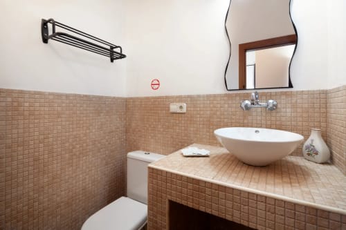Modern bathroom with beige tiled walls, white bowl sink, mirror, toilet, and towel rack in Málaga apartment