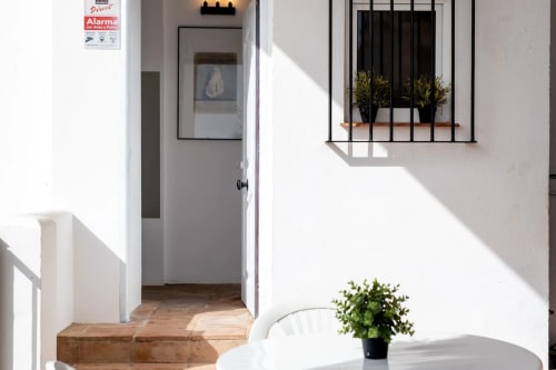 Bright white patio entrance at Apartamentos Turísticos Axarent, Málaga, with potted plants and barred window overlooking