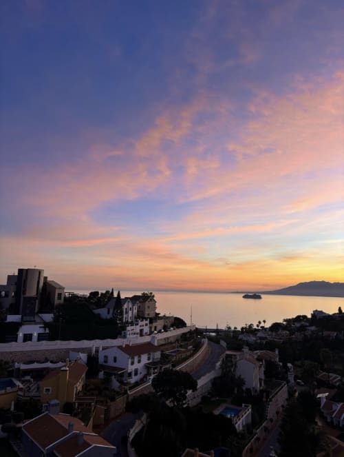 Sunset over Mediterranean Sea from Apartamentos Turísticos Axarent in Málaga with coastal town, white buildings and sailboat