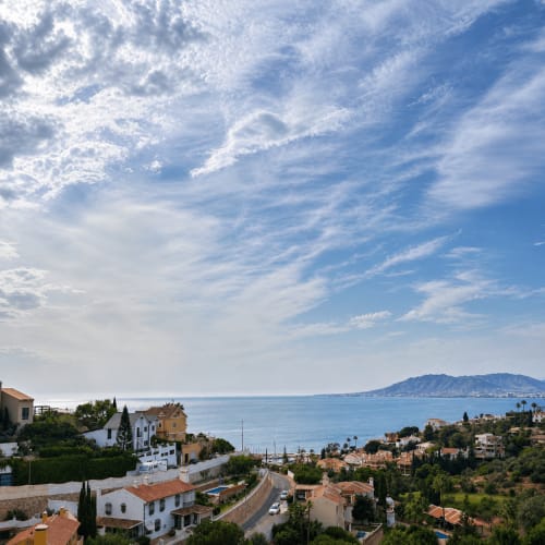 Coastal Málaga apartment complex with sea views, Mediterranean hillside homes, and distant mountains under blue sky