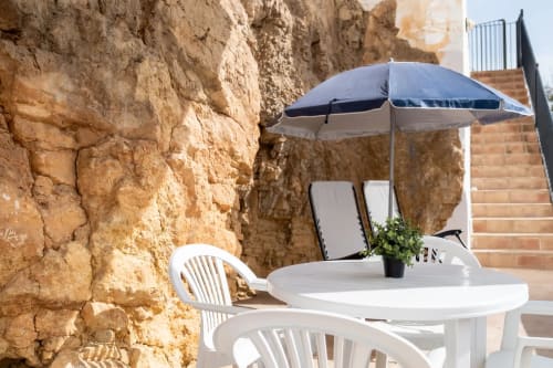Outdoor terrace at Apartamentos Turísticos Axarent in Málaga with white chairs, umbrella, and rustic stone architecture
