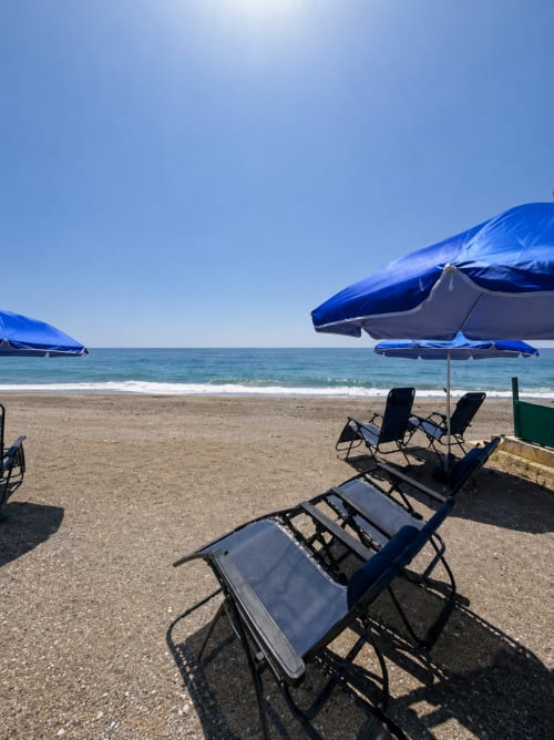 Blue beach umbrellas and lounge chairs on sandy beach at Almayate Alto with sea view and clear sky