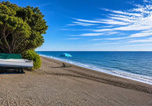 Almayate beach with blue umbrella, boat, and parasol on sandy shore under clear sky