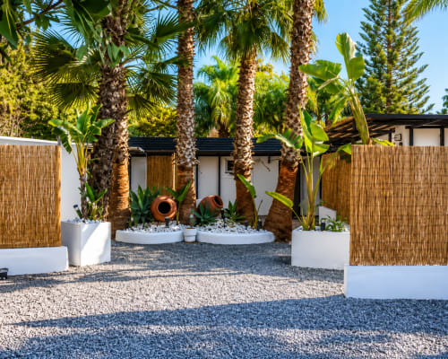 Tropical resort courtyard with palm trees, white planters, clay urns, gravel patio and wooden fences at Axarent Almayate