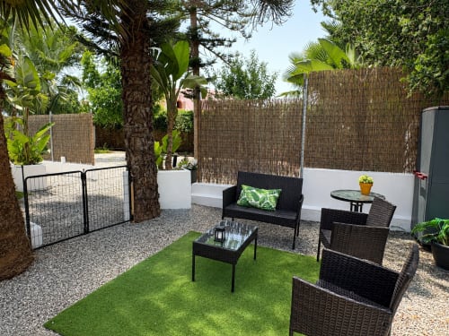 Outdoor patio seating area at Apartamentos Turísticos Axarent with black wicker furniture, green lawn, palm trees, and reed